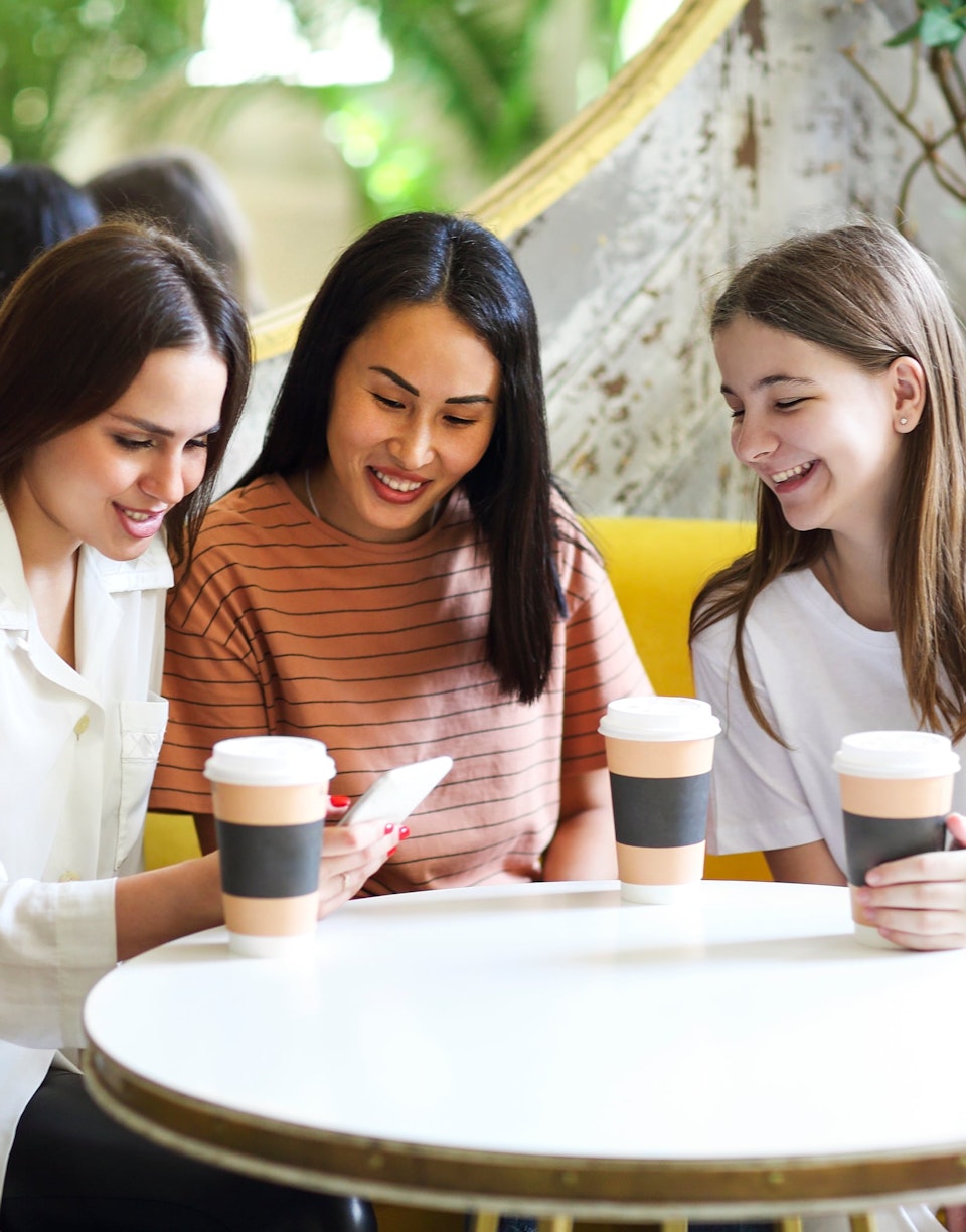 Chicas tomando café mientras consultan el smartphone