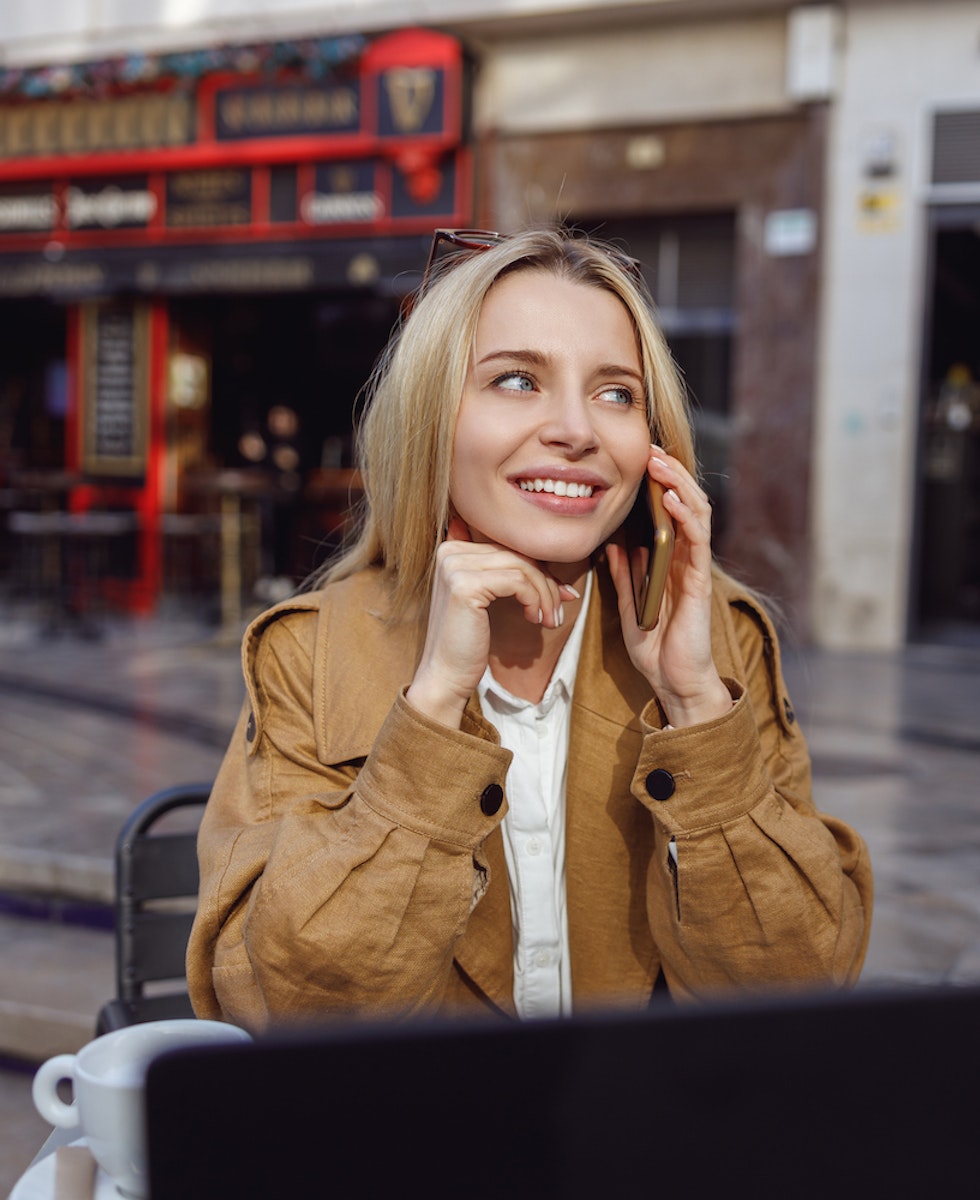 Mujer sentada en el exterior de una cafetería hablando por teléfono
