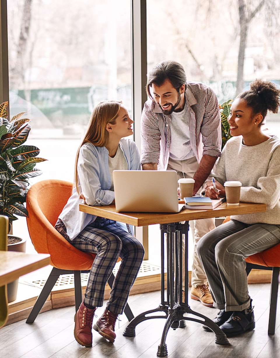 Personas conversando en una mesa con un ordenador y café.