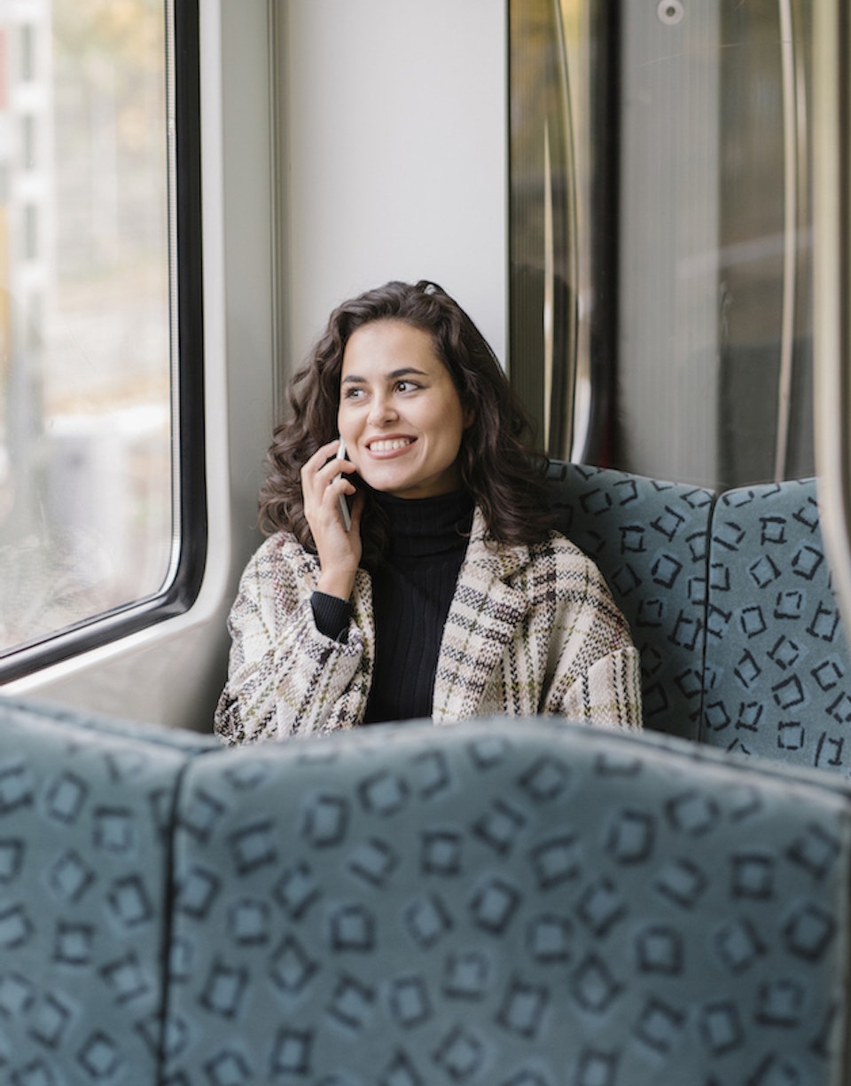 Mujer sonríe mientras habla por teléfono en un tren