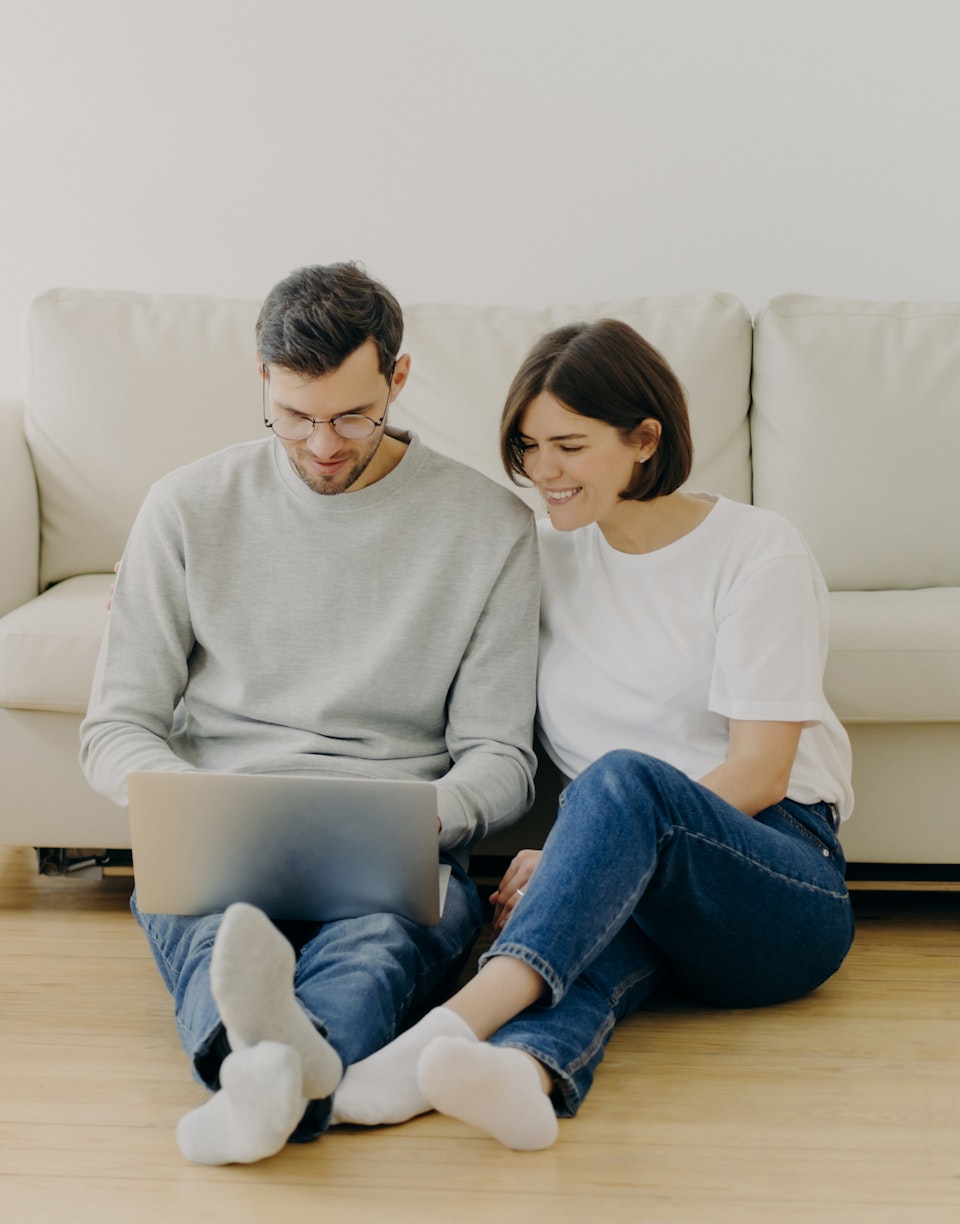 Pareja joven sentada en el suelo mirando un portátil