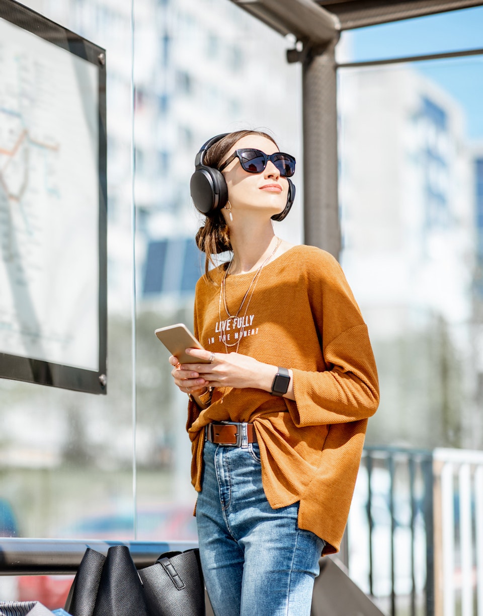 Mujer con auriculares, reloj inteligente y smartphone esperando el autobús.