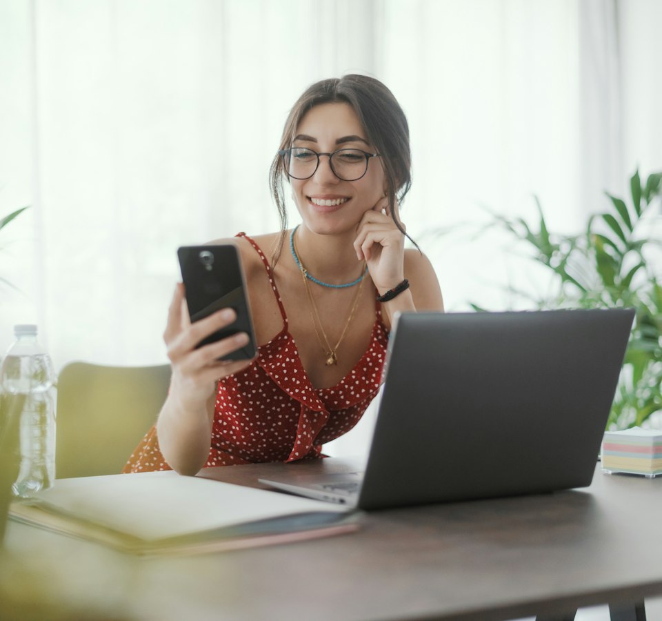 Mujer consulta su smartphone mientras teletrabaja.