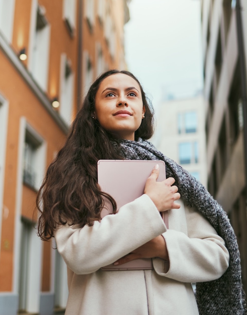 Mujer sonriendo mientras mira al horizonte y sostiene una tablet.